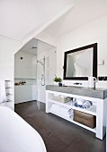 Contemporary, white bathroom with grey accents; washstand with concrete top below framed mirror on wall