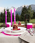 Dessertteller und pinkfarbene Kerzen auf festlich gedecktem Tisch, im Hintergrund Alpenblick