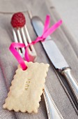 Biscuit used as name tag tied to silver cutlery with pink ribbon; fork decorated with raspberry