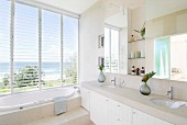 Moderne Waschzeile mit Steinplatte auf weissen Unterschränken, Stufe vor eingebauter Badewanne am Fenster mit Panoramablick
