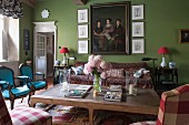 Rustic coffee table and chairs of various styles in green-painted, traditional living room with family portrait on wall