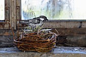 Hand-crafted paper bird in wicker birds' nest on windowsill