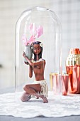 Figurine of Caribbean girl holding delicate summer flower under glass cover on white doily