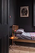 Black-painted bedroom with wooden bed, wooden floor and lit lamp and posy of roses on tray table