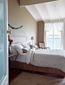 View through open door of double bed at comfortable height in rustic bedroom with taupe walls