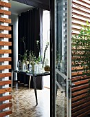 Blick durch Terrassentür in Wohnraum, Tisch mit verschiedenen Glasvasen und Blumenzweigen