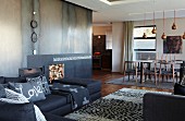 Offenes Wohnen im Designerstil - Sofakombination im Loungebereich mit Teppich, moderner offener Kamin mit Metallverkleidung im Hintergrund Essplatz