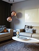 White, oval coffee table, pale grey sofa set and two spherical lamps with shiny copper lampshades in corner
