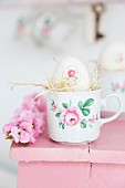 Easter egg decorated with napkin decoupage and straw in floral cup on pink footstool