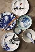 Arrangement verschiedener künstlerisch bemalter Teller und Schüsseln mit asiatischen Tiermotiven, Reislöffel und Essstäbchen
