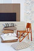 Subtle natural colours in interesting mixture of patterns - stack of cushions next to wooden chair and fabric-covered panels in background