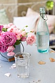 Roses of various colours in enamel pot, glass of water and vintage swing-top bottle on table