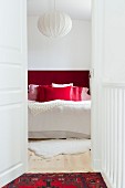 View through open door of double bed with headboard and scatter cushions in shades of red