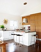 Delicate bar stools at free-standing kitchen island in open-plan, modern kitchen with wooden fronts