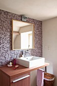 Modern, wooden washstand with countertop basin against mosaic-tiled wall