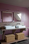 Modern washstand with twin, countertop basins, raffia baskets, mirrors and arched lamps on pale purple wall