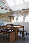 Retro stools and wooden bench with cushions around dining table in front of rustic brick wall in renovated interior