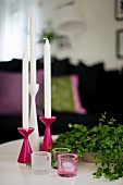 Mehrteiliges Kerzenständer-Set in Pink und Weiß, davor Windlichter, seitlich Schale mit Blätterzweigen