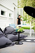 Black beanbags and side table in front of table under black parasol and woman in terrace door