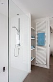 Shower area with glass screen, fitted shelving and white towel warmer on wall next to sliding door leading to toilet area