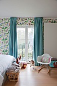 Nursery with classic rocking chair in front of window with light blue, floor-length curtains