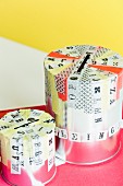 Empty paint tins decorated with washi tape and with slots in top used as money boxes