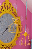 Pendant lamps with yellow-painted wire lampshades in front of vintage wall clock with ornate, yellow frame