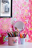 Beakers of pens on white surface, framed photo on pink wallpaper with floral pattern