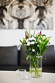 Garden flowers in glass vase and Alvar Aalto tealight holders on table with sofa below artwork in background