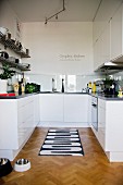 Black and white patterned rug on herringbone parquet floor in open-plan, white designer kitchen