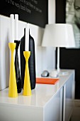 Group of white candles in colourful candlesticks on sideboard