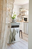 View through open doorway with white lace curtain into white country-house kitchen
