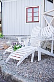 White wooden loungers on gravel terrace in front of wooden house with red window