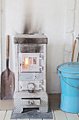 Old wood-burning stove next to blue metal bucket with lid in rustic interior