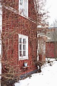 Rotbraunes Holzhaus und weiße Fenster mit verschneitem Garten