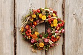 Autumnal wreath of everlasting flowers and fruits on wooden board wall
