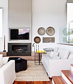 Seating group with pale upholstery in front of wall with integrated open fireplace and TV