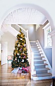 View through arched, open doorway of decorated Christmas tree next to white, wooden staircase in foyer