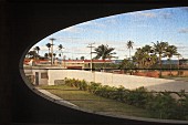 Oval window aperture in concrete facade with view of palm trees in urban setting