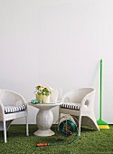 weiße Rattan Gartenmöbel auf Kunstrasen, verschiedene Gartenutensilien und Geräte vor weisser Wand