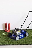 Lawn-mower and gardening equipment on artificial lawn against white wall