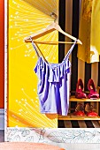 Top hanging on coathanger against white and yellow panel of wardrobe door and shoes on shelves