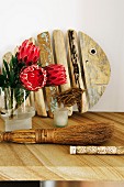 Proteas in vase and rustic hand brush on table in front of wooden fish sculpture leaning against wall
