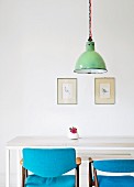 Hand-crafted dining table and chairs with blue upholstery below vintage pendant lamp in front of framed postcards on wall