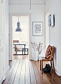 Flea-market vases and chair in bright corridor of period apartment; view of industrial lamp above DIY dining set through door at far end