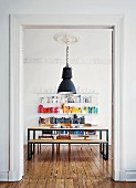 DIY, chipboard dining set with black frames below vintage industrial lamp hanging from stucco ceiling in front of colourful books on shelving