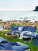 Casual outdoor furniture with metal frames and blue-covered cushions on stony sea shore