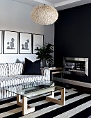 Black and white, Scandinavian-style seating area; sofa and glass table on rug with wide stripes in front of chimney breast painted anthracite grey