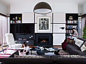 Children in modern living room with black corner sofa and open fireplace