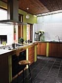Base units with wooden doors and side walls painted lime green in 60s fitted kitchen; bar stool in front of gas cooker with extractor hood